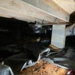 Thumbnail image of Crawl space with exposed soil, a damaged vapor barrier, concrete support piers, and wooden floor joists overhead, showing moisture-related deterioration and conditions that may require encapsulation or foundation repairs.