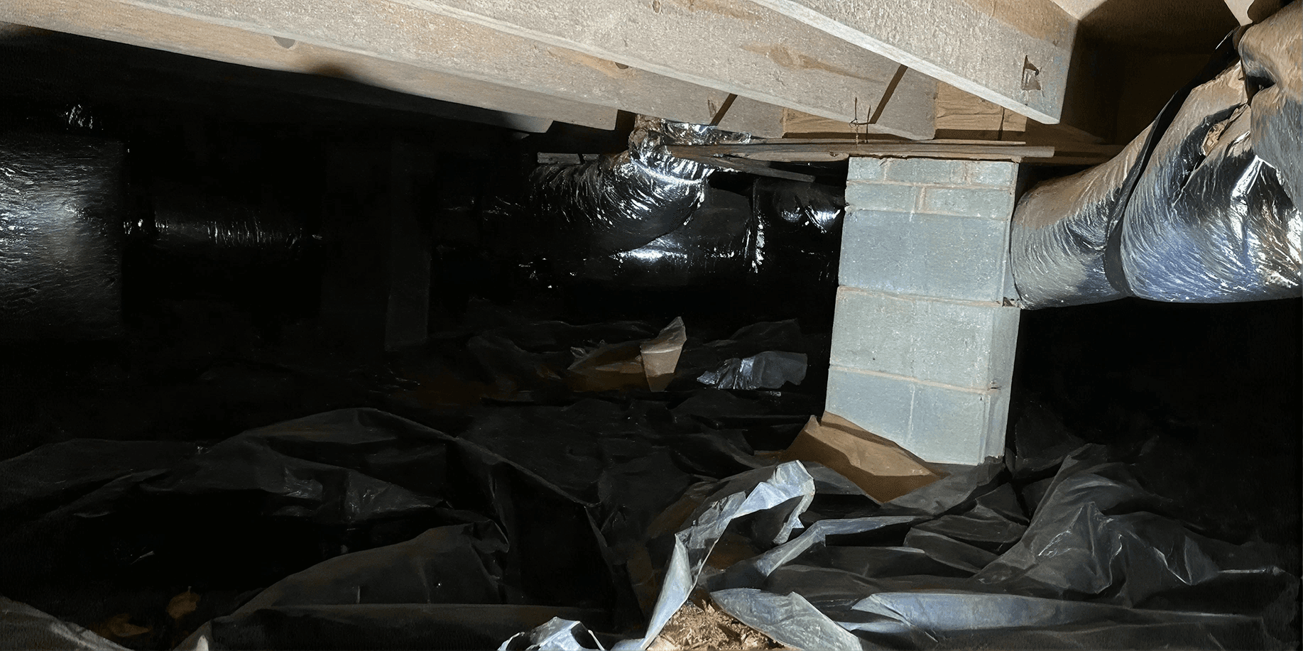 Dark crawlspace with a torn and displaced vapor barrier, exposed dirt, and visible ductwork, showing moisture control issues before encapsulation.