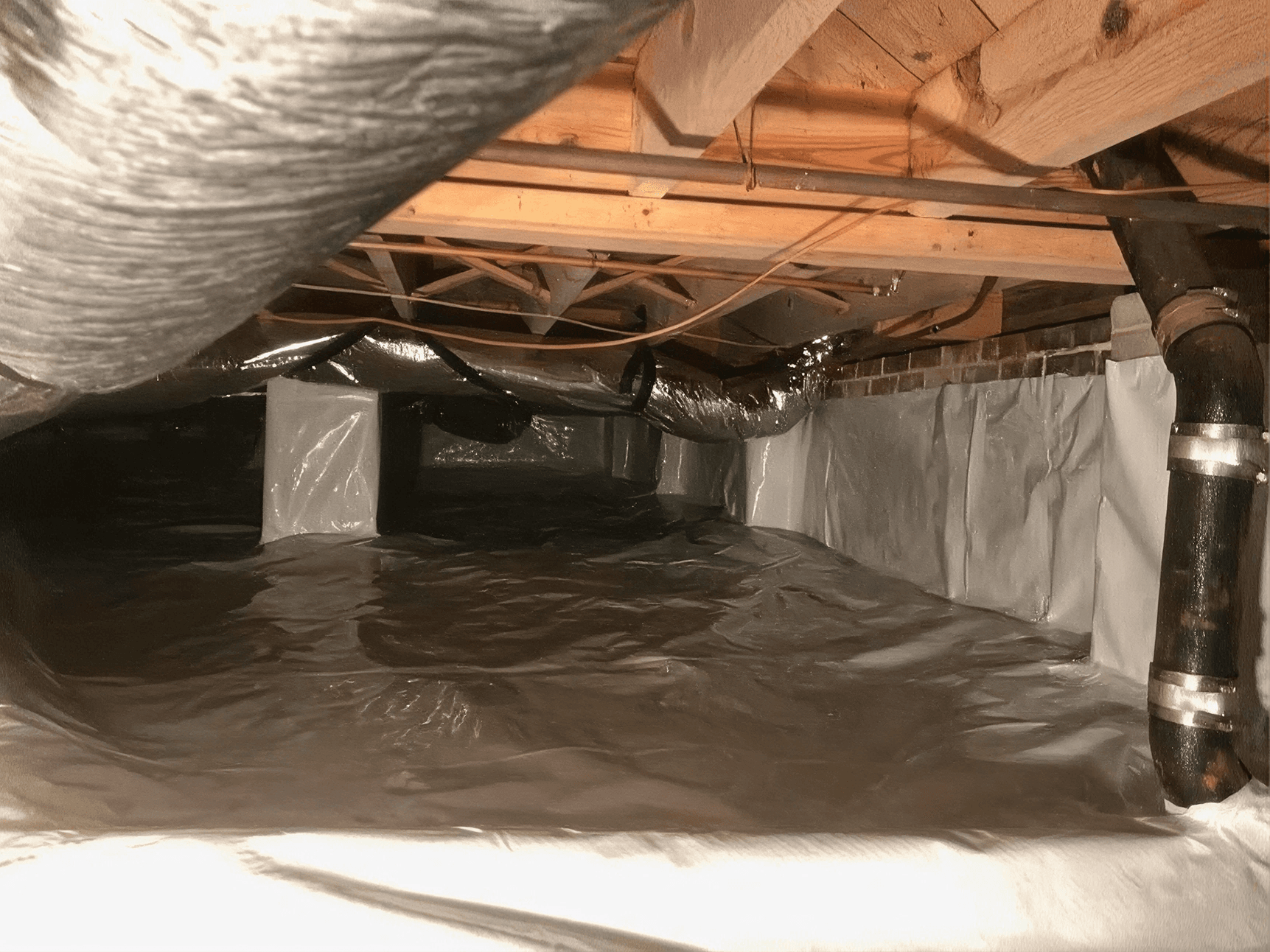 Clean crawlspace after encapsulation with sealed white vapor barrier covering the floor, walls, and support piers beneath exposed ductwork.