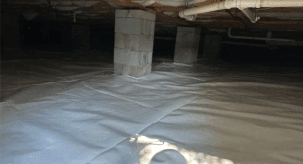 Dim unfinished basement with concrete support pillars, exposed ceiling pipes, and a white plastic vapor barrier covering the floor.