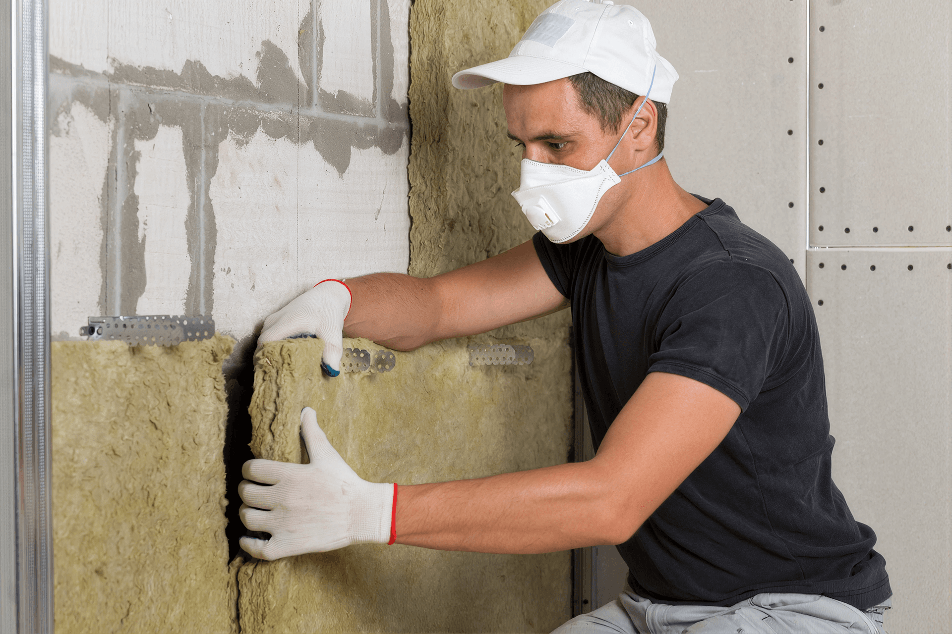Technician wearing protective gear installing fiberglass insulation batts inside an unfinished wall to improve energy efficiency and indoor comfort.