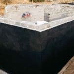 Thumbnail image of Exterior foundation wall coated with a waterproof membrane to help prevent moisture penetration and protect the basement from water intrusion before backfilling.