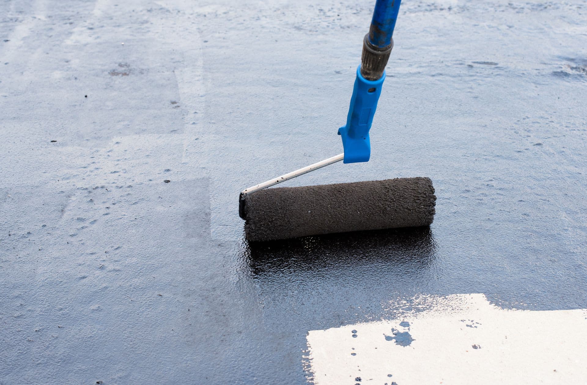 Close-up of a waterproof coating being applied with a paint roller to create a protective moisture barrier on a concrete foundation surface.