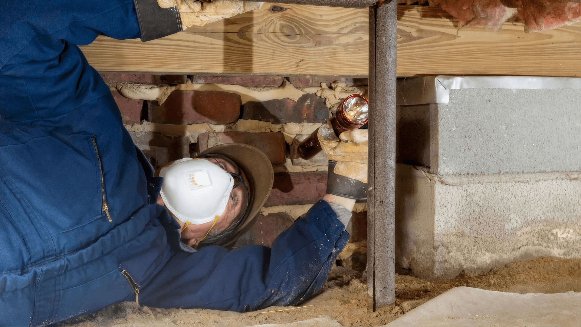 Crawlspace inspector examining the foundation and structural supports with a flashlight.