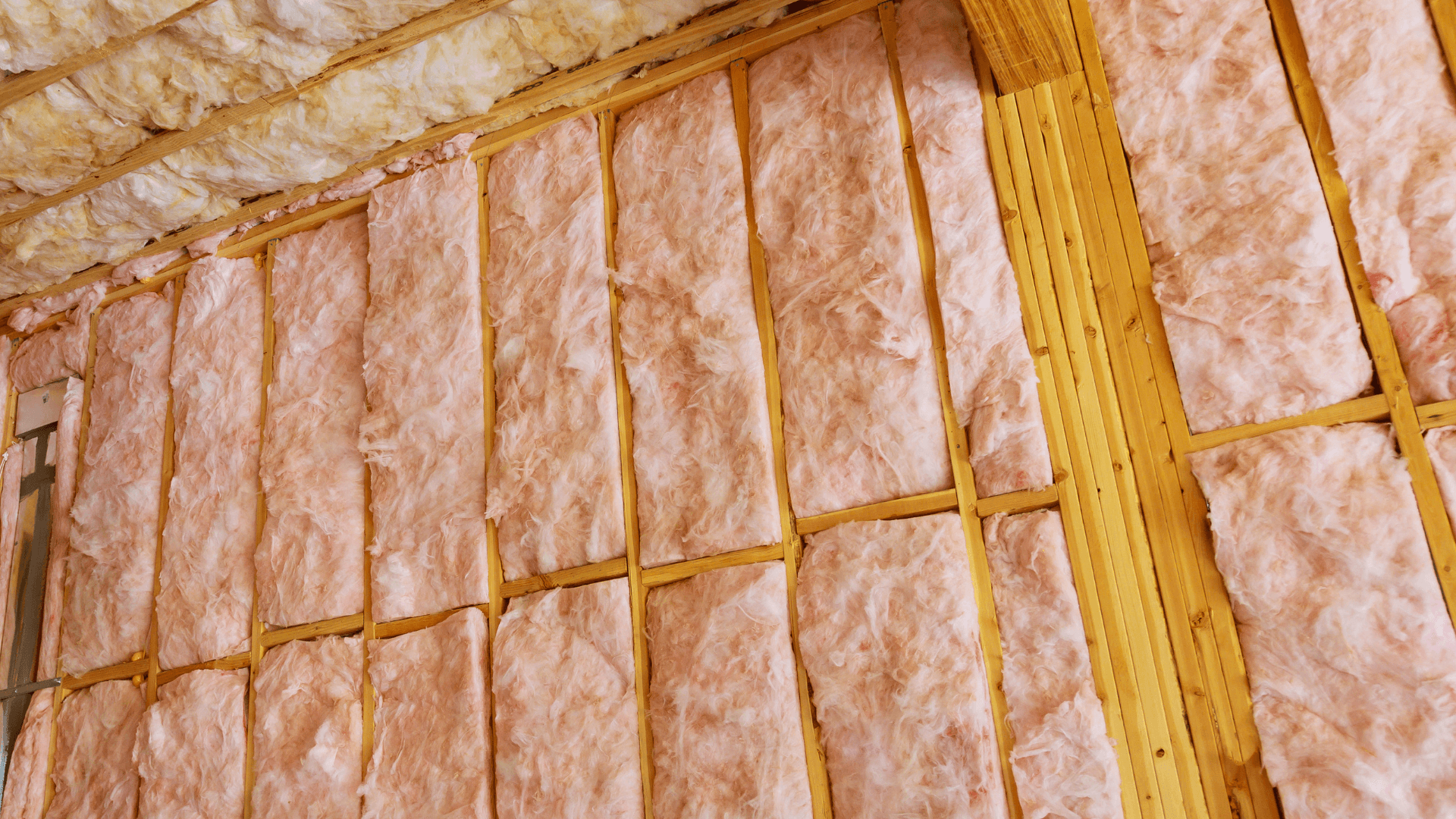 Exposed wooden wall studs filled with pink fiberglass insulation in an unfinished interior, highlighting home construction and warm earthy tones.