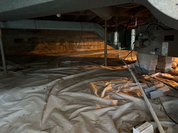 Crawlspace with a partially installed or aging vapor barrier, exposed ductwork, support posts, wiring, and HVAC equipment.