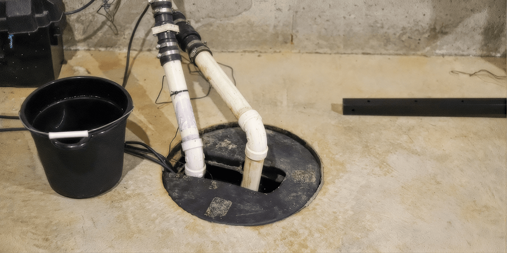 Basement sump pump basin with connected discharge pipes and electrical components installed in a concrete floor, designed to collect and pump groundwater away from the home's foundation.