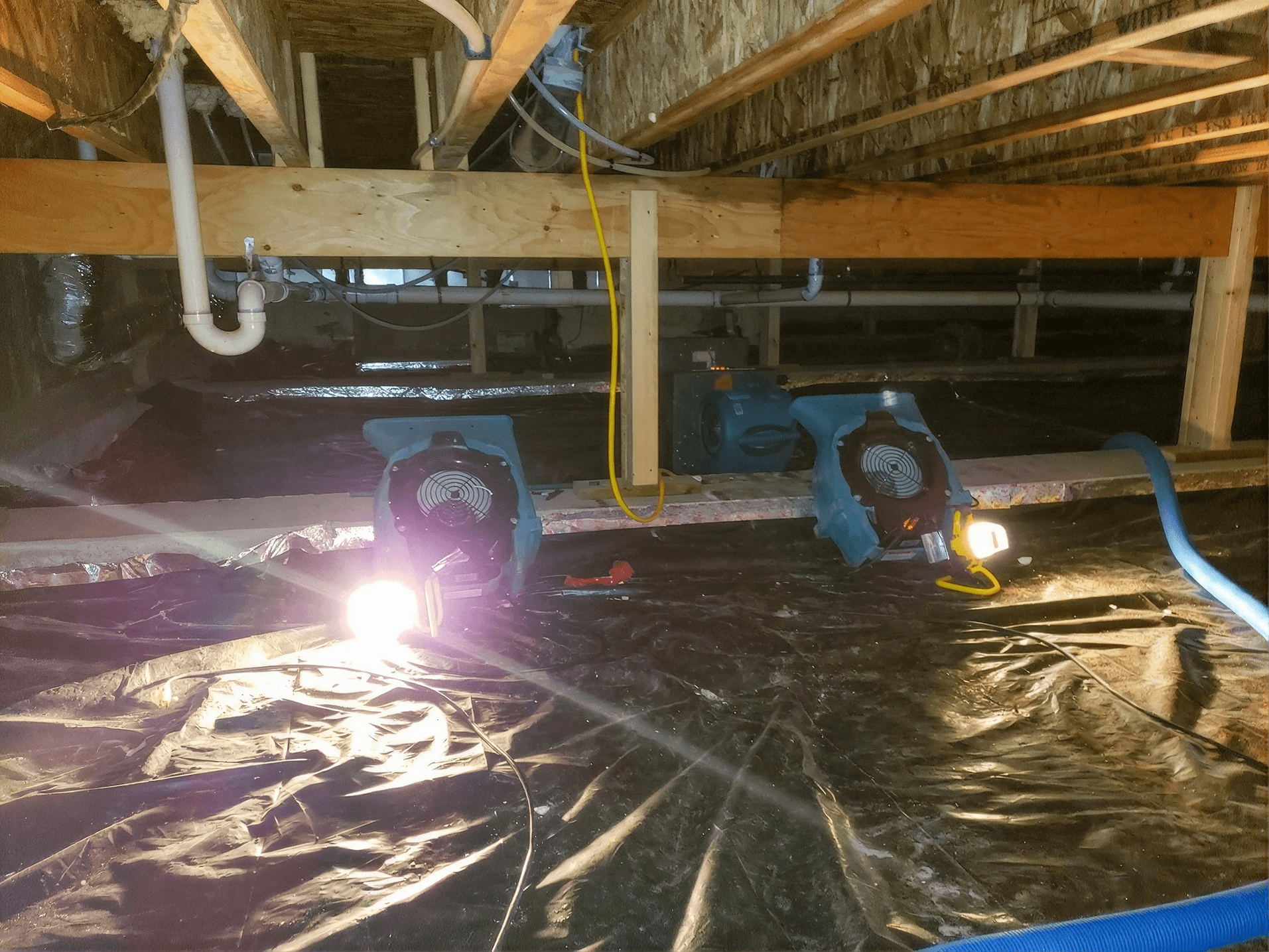 Crawl space with heavy-duty vapor barrier installed and commercial air movers operating to dry the area after water intrusion, helping remove excess moisture before encapsulation or restoration work is completed.