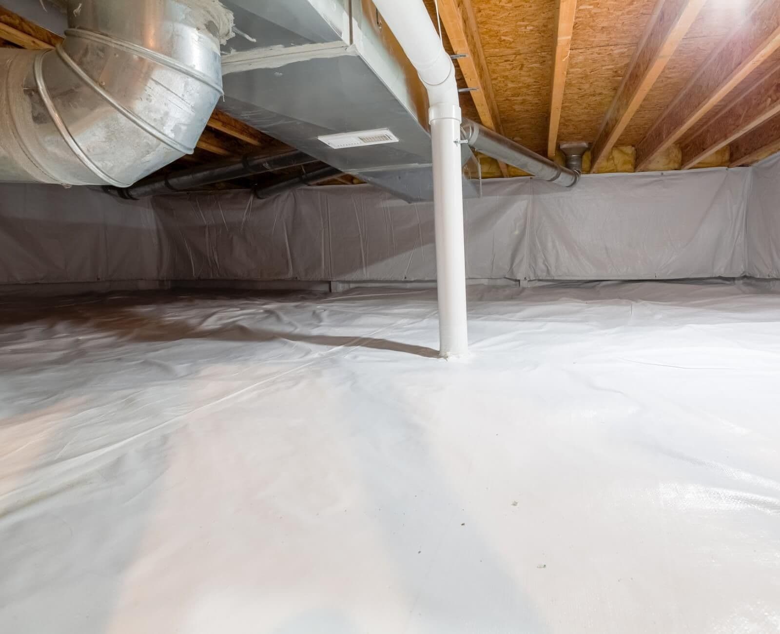 Encapsulated crawl space with a clean white vapor barrier covering the floor and walls, exposed wooden floor joists overhead, HVAC ductwork, plumbing lines, and a central support column, creating a dry and protected under-home environment.