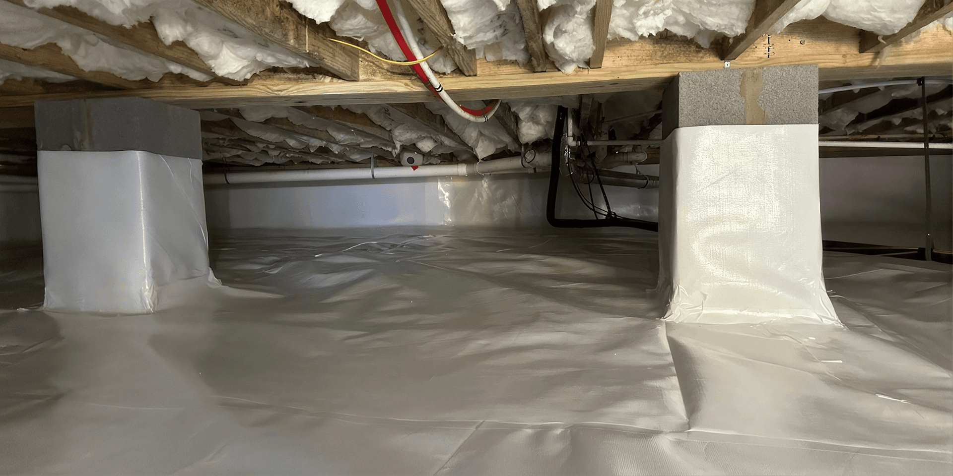Finished crawlspace encapsulation with a sealed white vapor barrier covering the floor, foundation walls, and support columns.