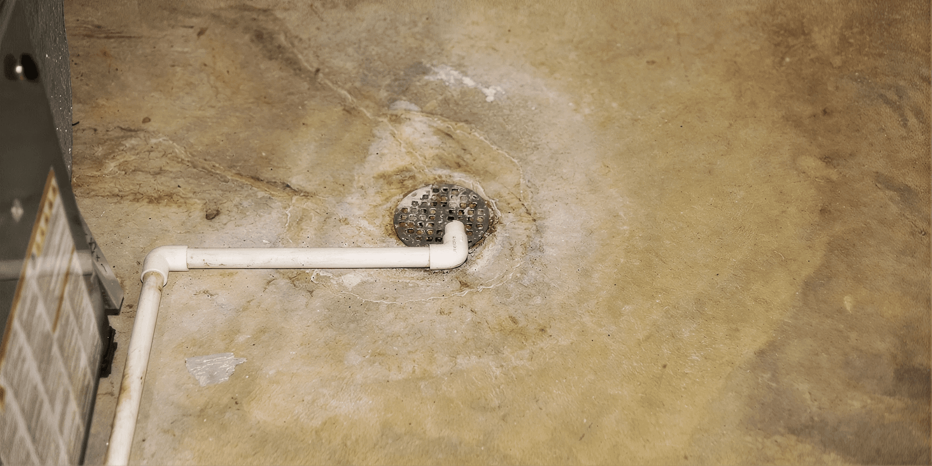 Close-up of a basement floor drain with a nearby condensate drain line, showing the drainage system used to help direct excess water away from the foundation and reduce the risk of basement flooding.