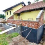 Thumbnail image of Exterior of a home's foundation with black waterproofing membrane applied below grade around the foundation walls during construction, helping protect the basement from moisture intrusion and water damage.