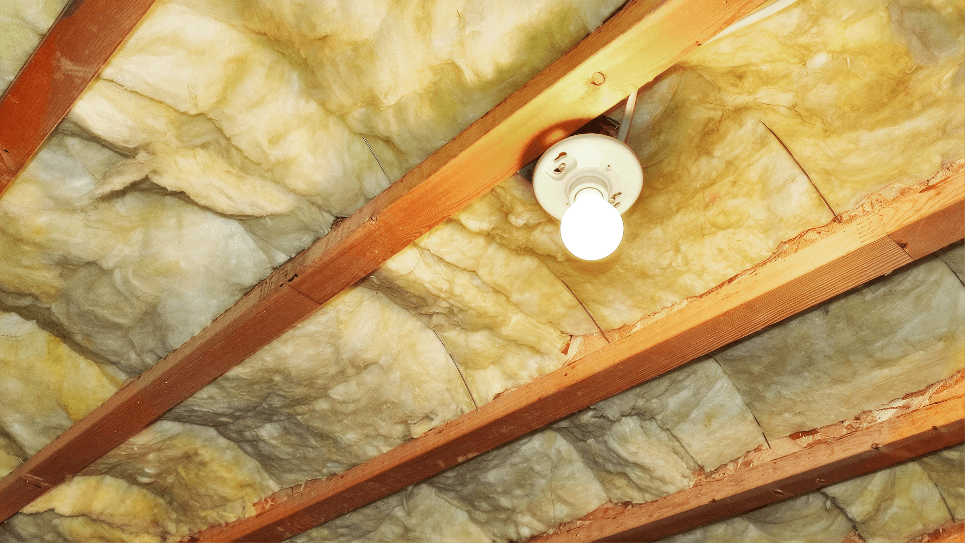 Exposed fiberglass insulation installed between wooden floor joists in a crawlspace.